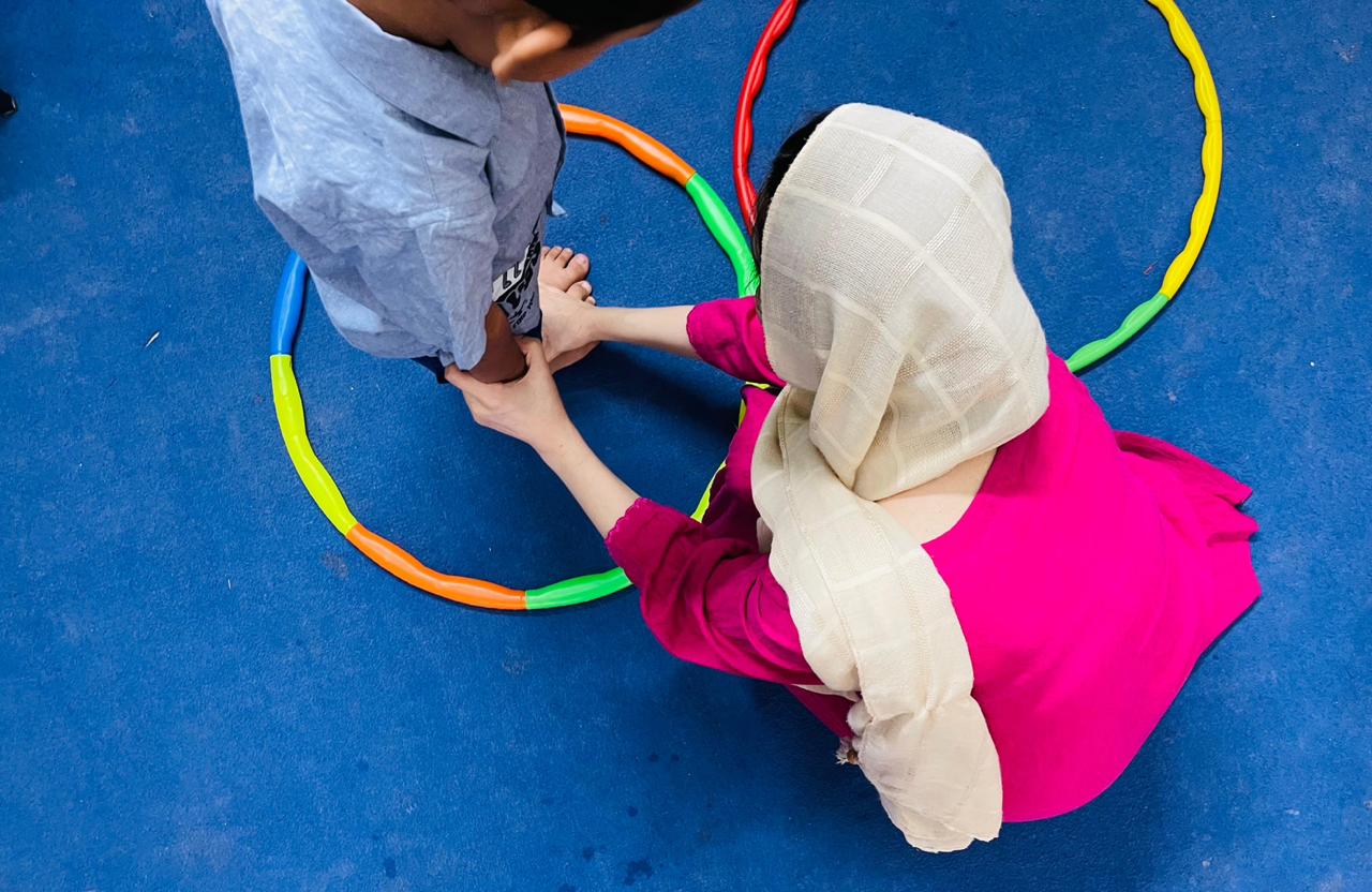 Therapist guiding child through hula hoop coordination exercise at Global Kids Campus Therapy Centre Lahore
